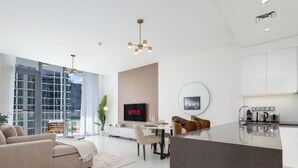 Una sala de estar moderna con sofá, mesa de comedor y sillas, una cocina con televisor y cafetera, y ventanas amplias con vistas a la ciudad.