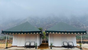 Two tents with white walls and green roofs, each with a small table and chair, set against a mountainous backdrop. - Pushkar Dhani Camps And Resort (Pushkar)