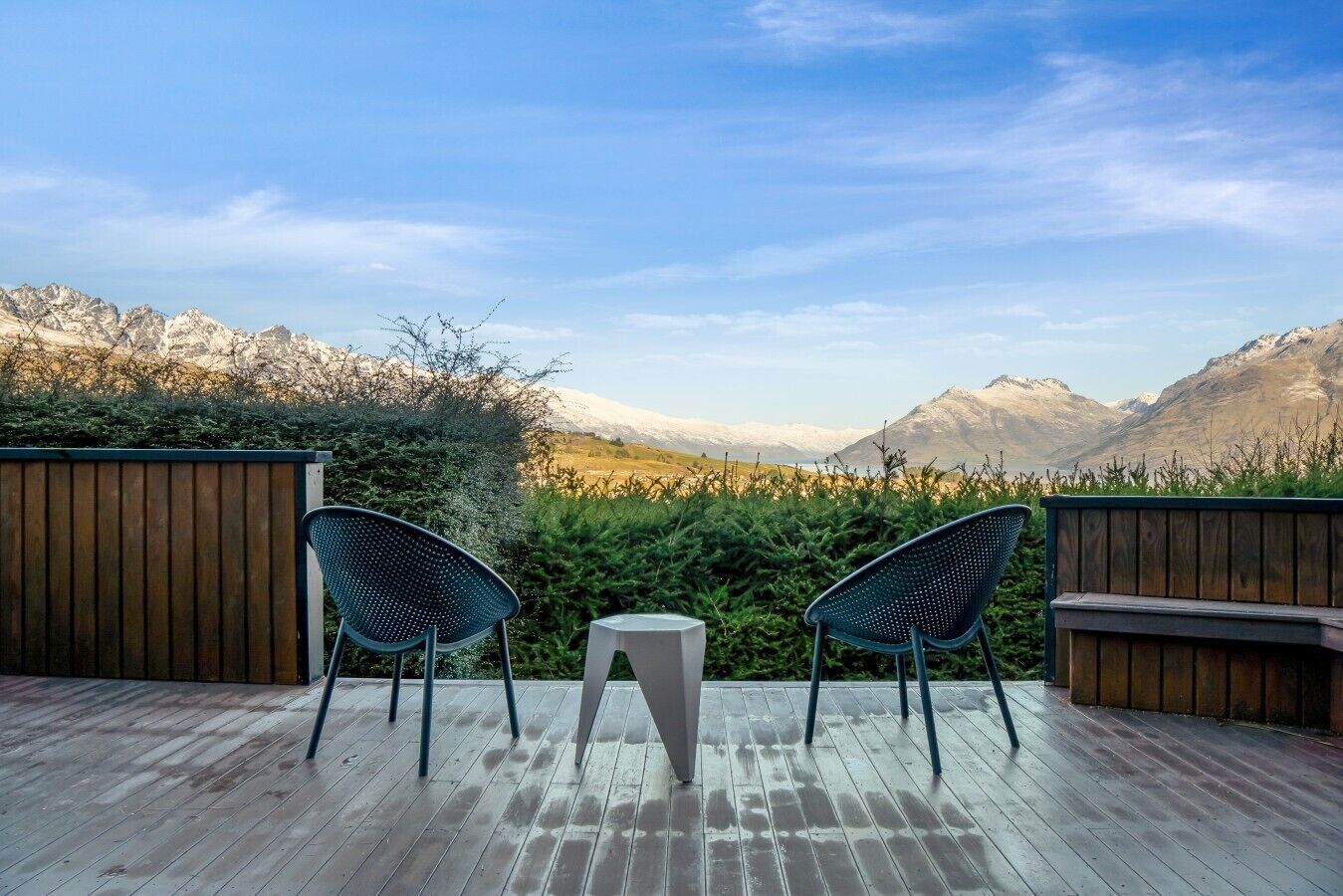 Eine Holzterrasse mit zwei Stühlen und einem kleinen Tisch mit Blick auf eine Berglandschaft.