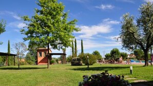 A grassy area with a small red building, possibly a gazebo, surrounded by trees and a clear sky.