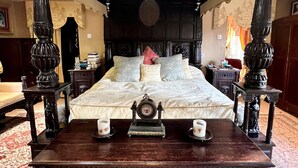 Una cama con dosel de madera oscura con intrincados adornos, una mesita de noche a juego y un reloj decorativo.