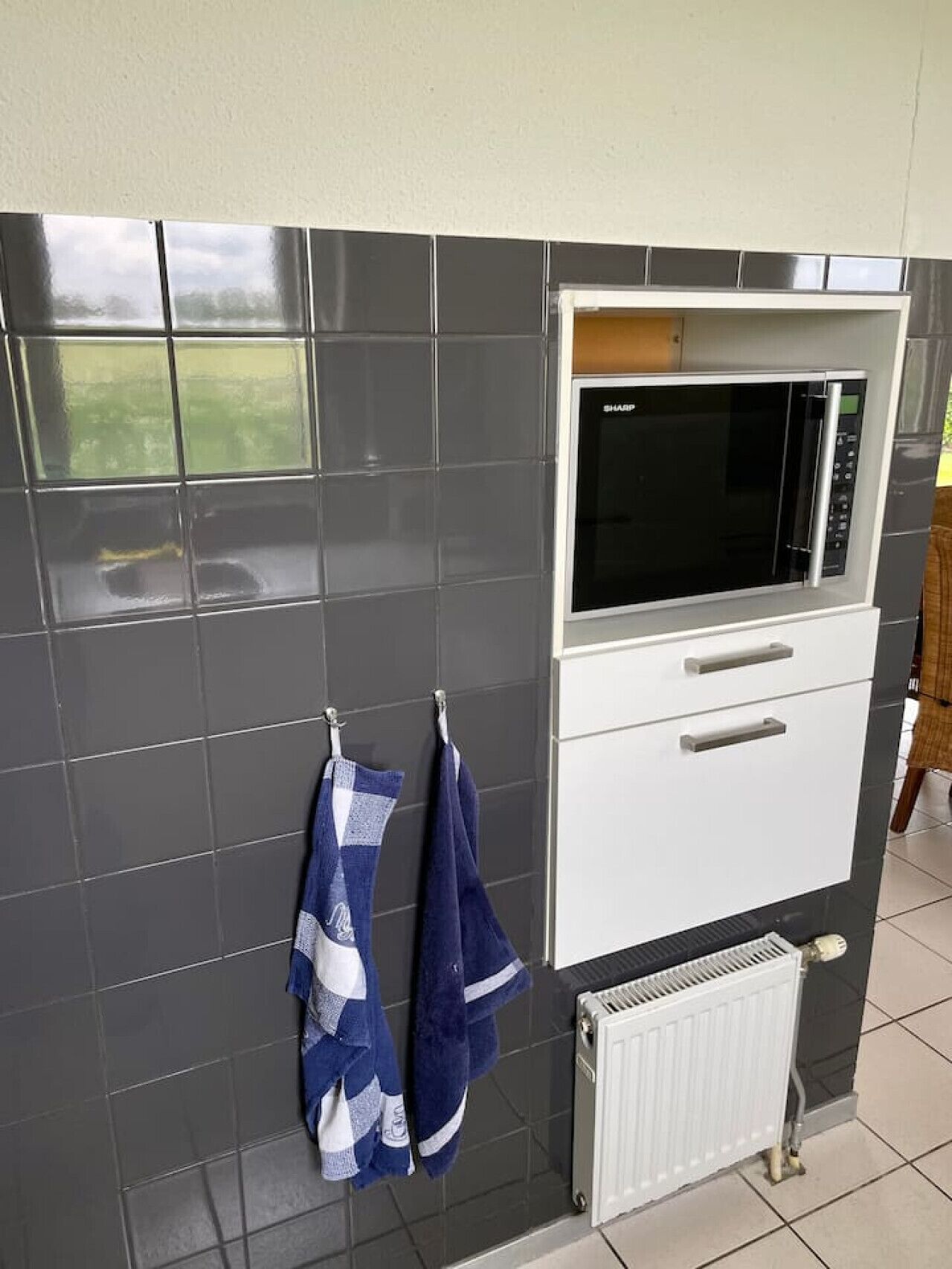 Une cuisine avec des carreaux gris foncé, un micro-ondes blanc et un meuble blanc en dessous.