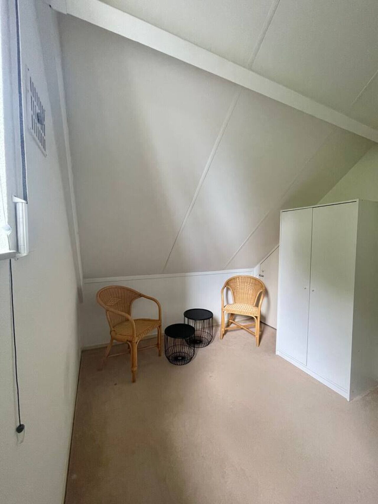 Une petite pièce aux murs blancs, avec deux chaises en osier et deux petites tables rondes noires.