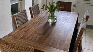 A dining area with a wooden table, wicker chairs, a vase with flowers, and pendant lighting. - Compleet huisje tussen de weilanden in Ewijk (Ewijk)