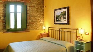 Una camera da letto con soffitto in mattoni, parete in pietra, un letto con copriletto, un comodino con lampada e un quadro appeso al muro.