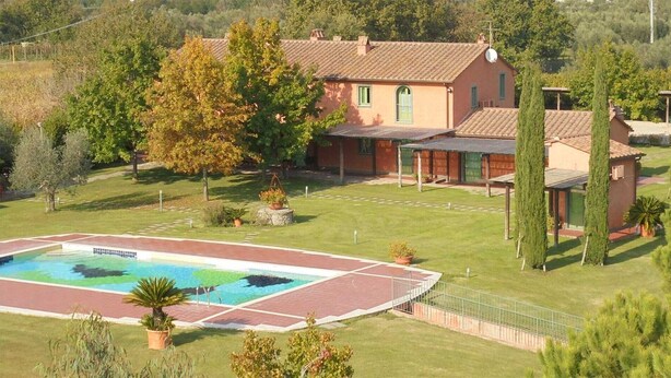 Una casa circondata da alberi e un prato curato, con una piscina.