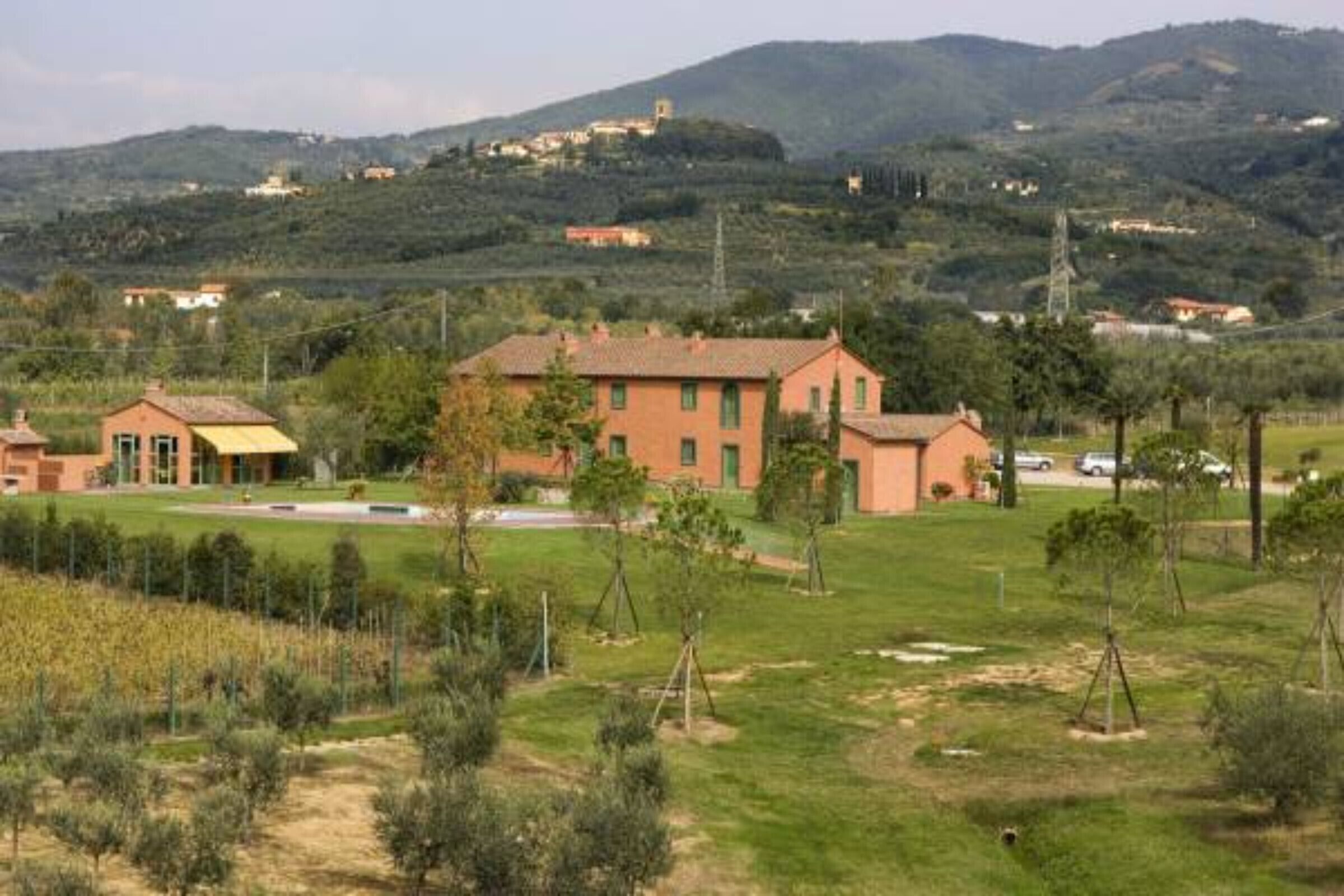 A rural setting with a large house surrounded by greenery and a hilly landscape in the background.