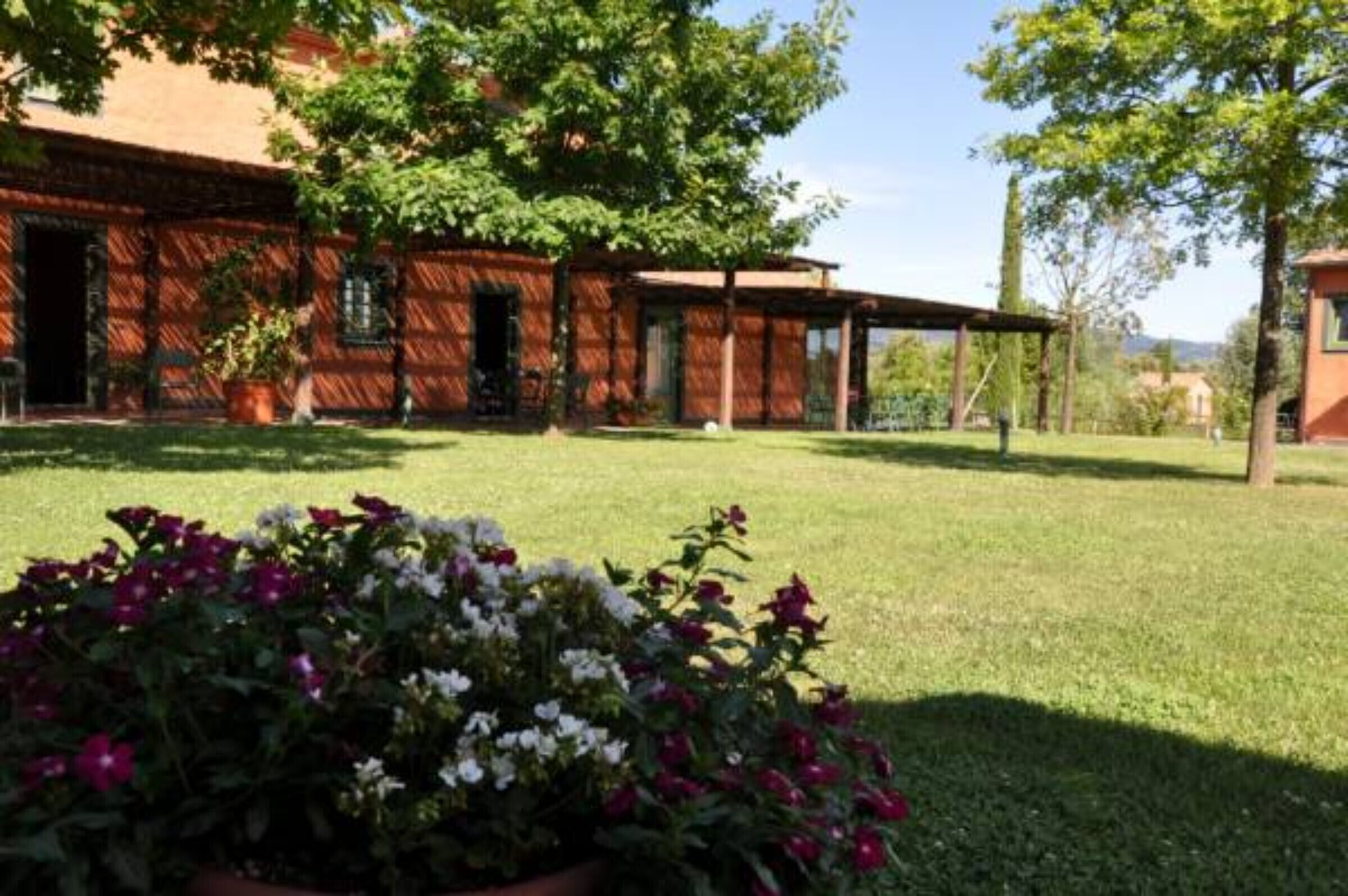 A rustic building with a covered patio, a lawn, and flowering plants in the foreground.