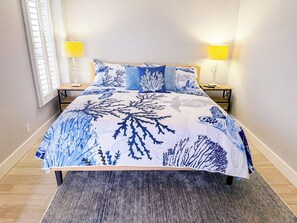 A bed with a blue and white coral print bedspread, two bedside lamps, and a window with blinds. - Sea Marsh I 404 (North Myrtle Beach)
