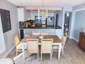 A modern kitchen with white cabinets, a central island, and a dining area with a wooden table and chairs. - Sea Marsh I 404 (North Myrtle Beach)