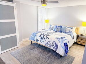 A bedroom with a bed, bedside lamps, a nightstand, a window with blinds, and a ceiling fan. - Sea Marsh I 404 (North Myrtle Beach)