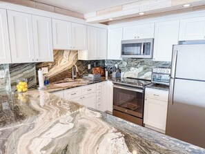 A kitchen with white cabinets, a marble countertop, a microwave, an oven, and a refrigerator. - Sea Marsh I 404 (North Myrtle Beach)