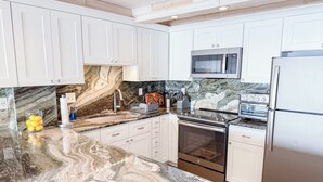 Una cocina con gabinetes blancos, encimera de mármol, horno de acero inoxidable, microondas y refrigerador.