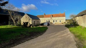 A rural stone building with a red-tiled roof, a gravel driveway, and a parked car.