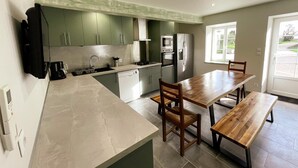 A modern kitchen with green cabinets, a wooden dining table, and a built-in oven.