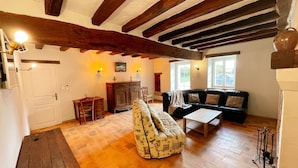 A cozy living room with exposed wooden beams, a sofa, a patterned armchair, and a wooden coffee table.