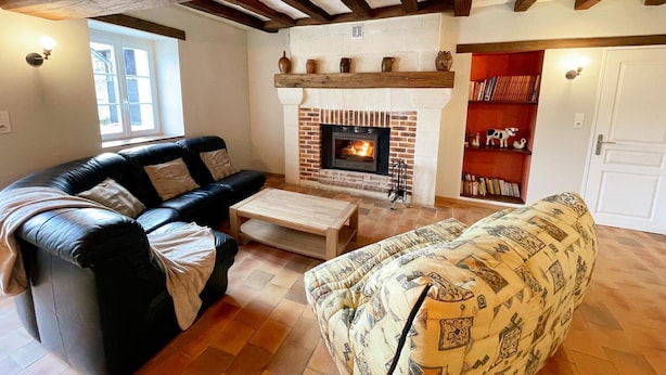A living room with a fireplace, a black leather sofa, a patterned armchair, and a bookshelf.
