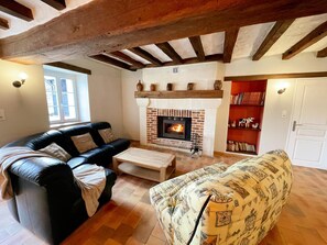 A living room with a fireplace, a black leather sofa, a patterned armchair, and a bookshelf. - Cozy cottage with WIFI, parking, air conditioning in Touraine (Gizeux)