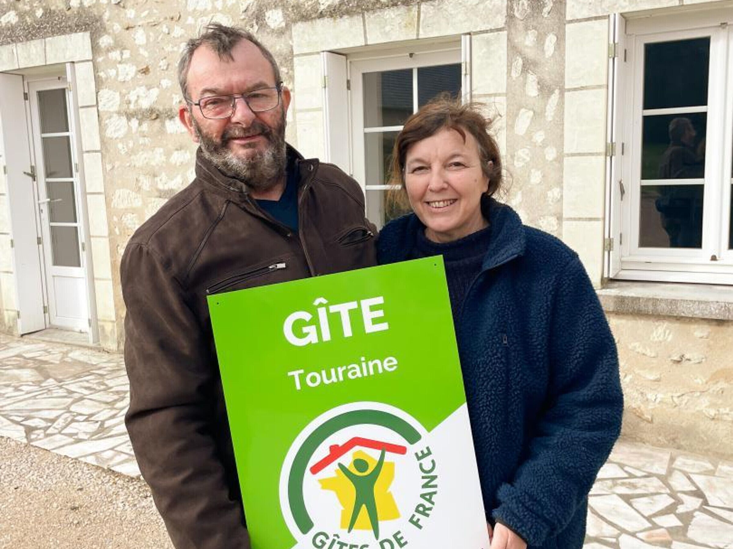 Due persone che tengono un cartello con i loghi "GÎTE Touraine" e "GÎTE DE FRANCE".
