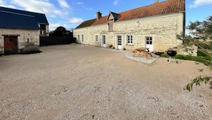 A stone building with a gravel courtyard, a wooden bench, and a barbecue grill.