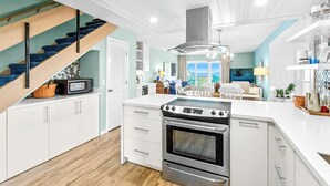 Eine moderne Küche mit weißen Schränken, einem Backofen und einer Mikrowelle. Eine Treppe mit blauem Teppich führt zu einer weiteren Ebene.