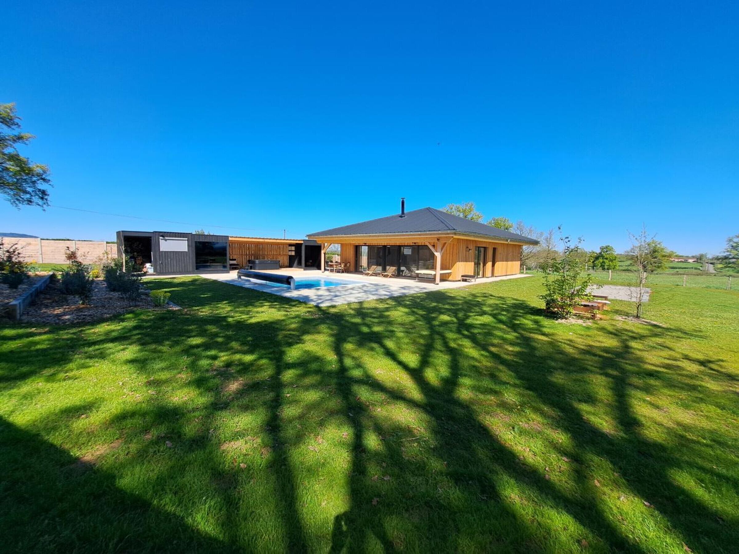 Een modern huis met een zwembad, een overdekt terras en een verzorgd gazon.