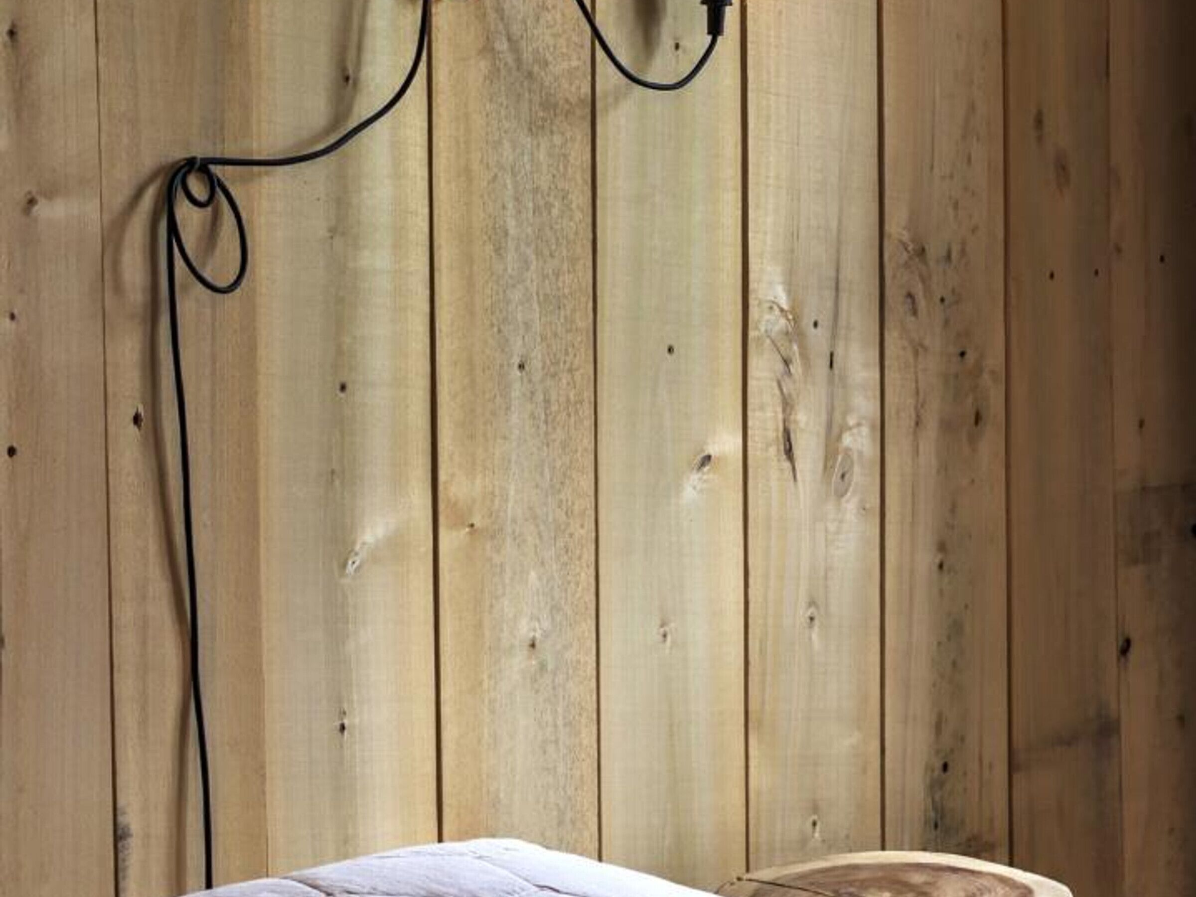 Eine Holzwand mit einem daran hängenden schwarzen Kabel.