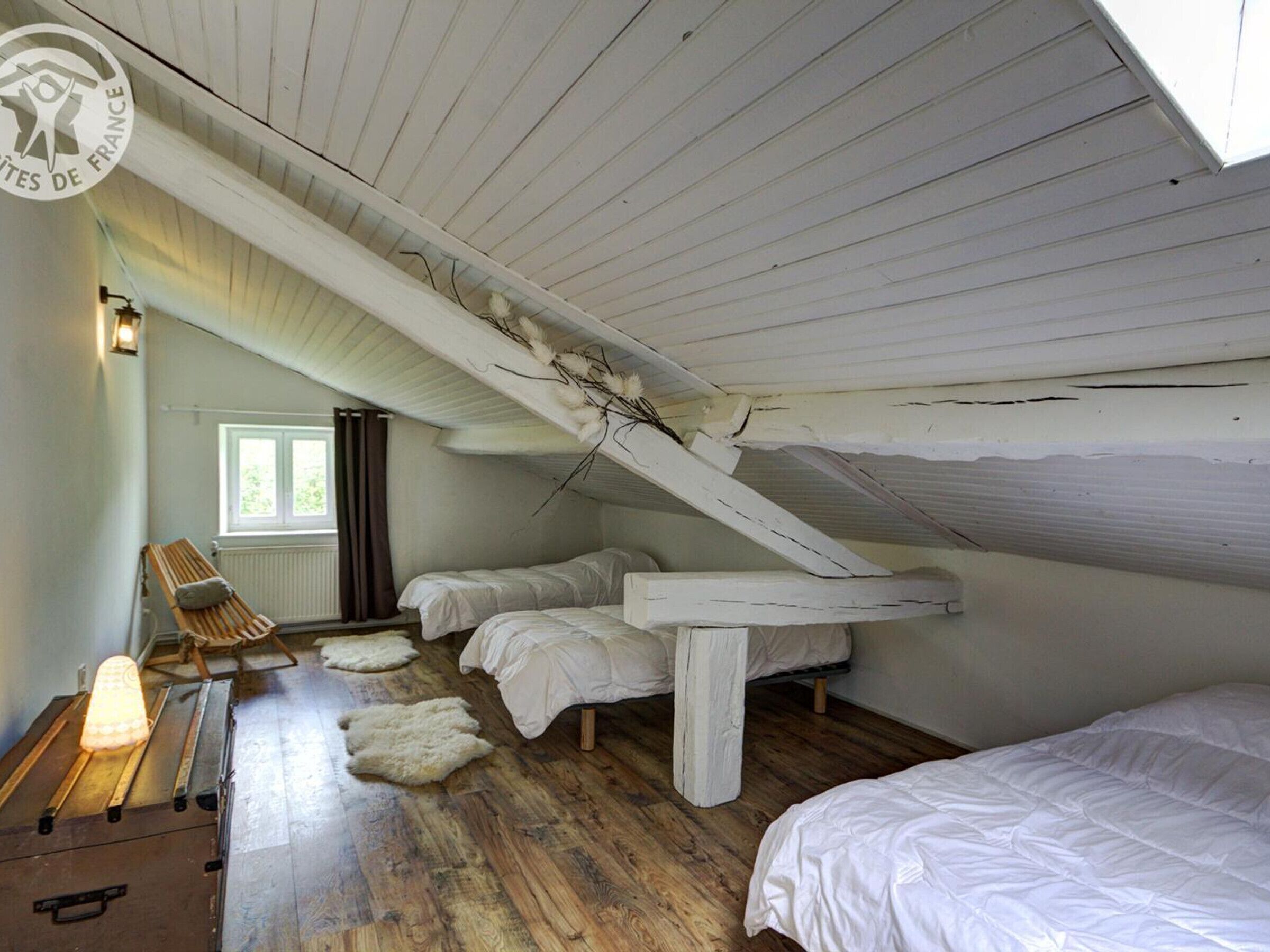 Un dormitorio rústico en un ático con vigas de madera, dos camas, un banco y un radiador.