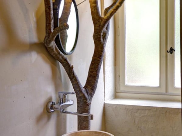 A bathroom with a tree-shaped mirror, a sink, and a window.