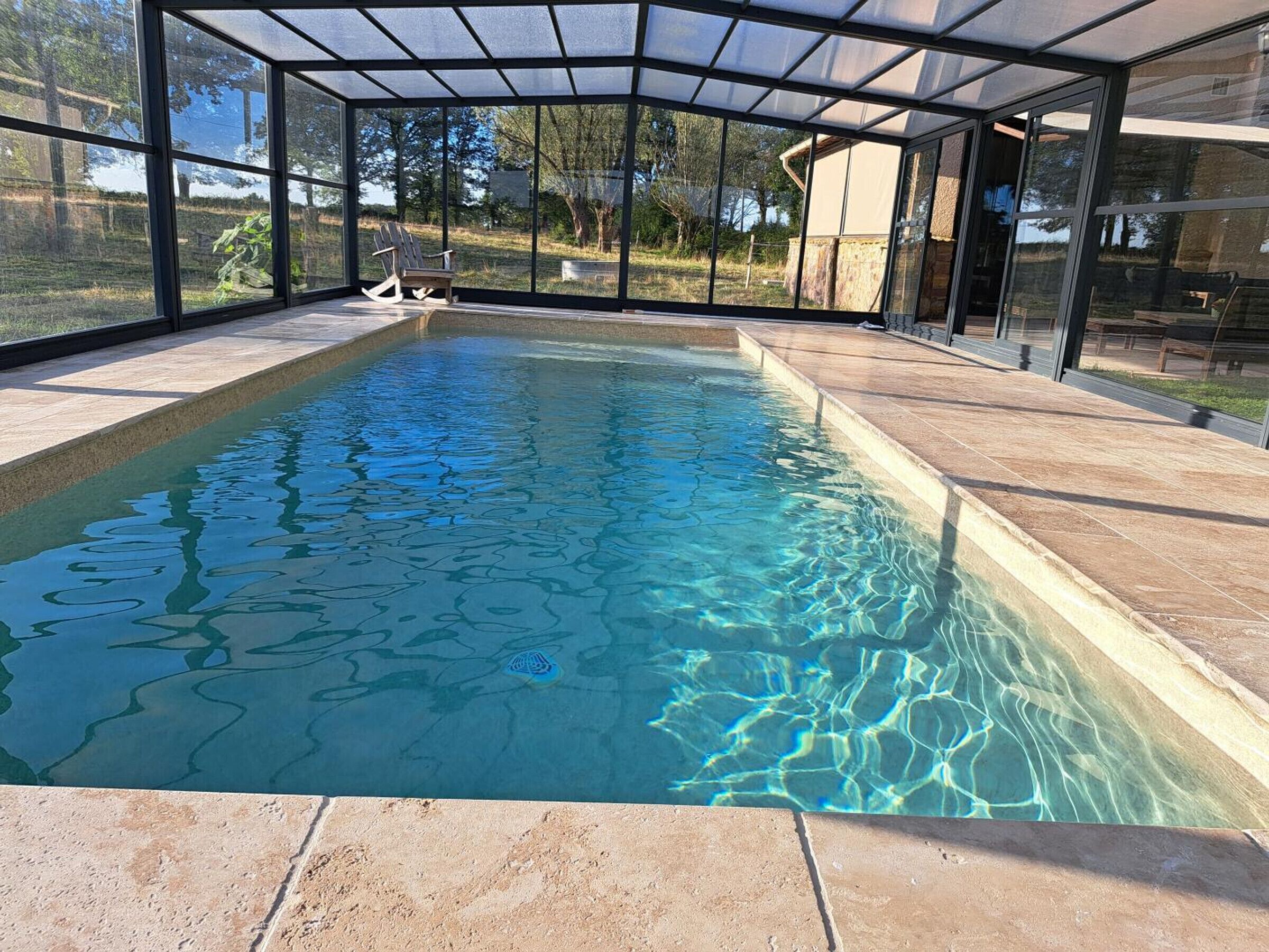 A swimming pool with a glass enclosure, surrounded by a patio area.