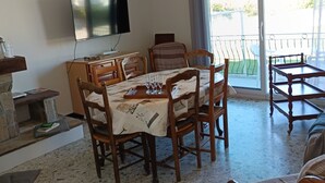 Ein Essbereich mit einem für vier Personen gedeckten Tisch, einem an der Wand montierten Fernseher und Blick ins Freie durch eine Schiebetür.