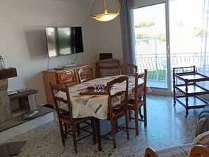 Ein Essbereich mit einem für vier Personen gedeckten Tisch, einem an der Wand montierten Fernseher und Blick ins Freie durch eine Schiebetür.