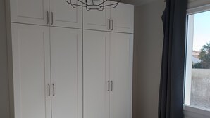 Ein Zimmer mit weißen Schränken, einem fenster mit Vorhängen und einer Deckenleuchte.