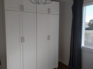 Ein Zimmer mit weißen Schränken, einem fenster mit Vorhängen und einer Deckenleuchte.