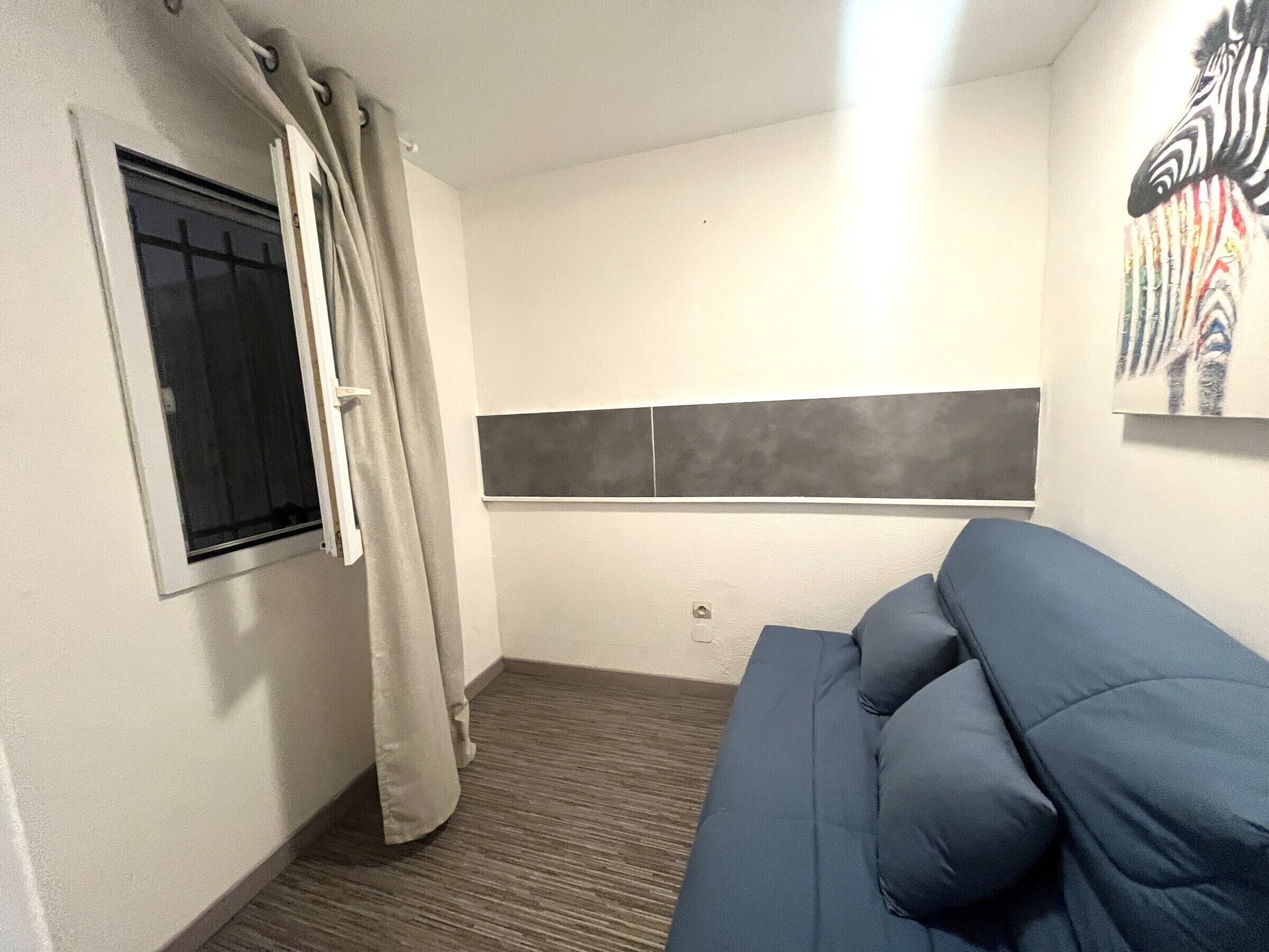 A room with a blue sofa, a window with a curtain, a wall-mounted artwork, and a grey accent wall.