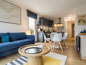 A modern living room with a blue sofa, a wooden coffee table, and a dining area with white chairs. - Charming apartment with large terrace in La Baule (La Baule)