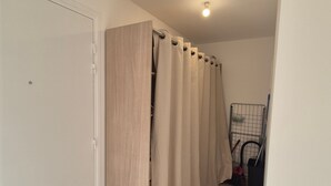 En hall med en trädörr, beige gardiner och ett metallställ med städmaterial.