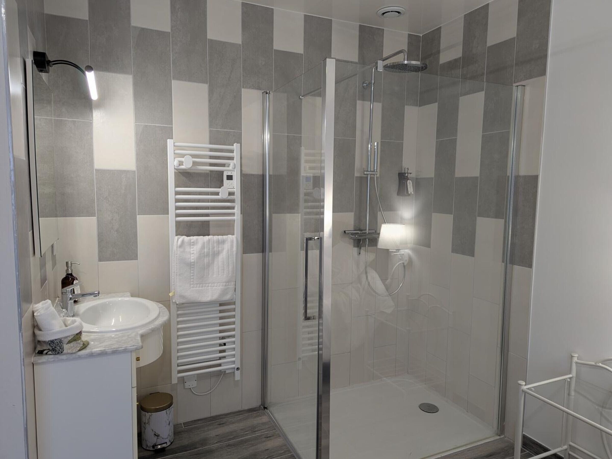 Uma casa de banho moderna com chuveiro em cabine de vidro, lavatório branco e suporte para toalhas.
