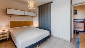 Ett modernt hotellrum med en stor säng, ett nattduksbord med en lampa, en vägghylla och utsikt över omgivningarna.