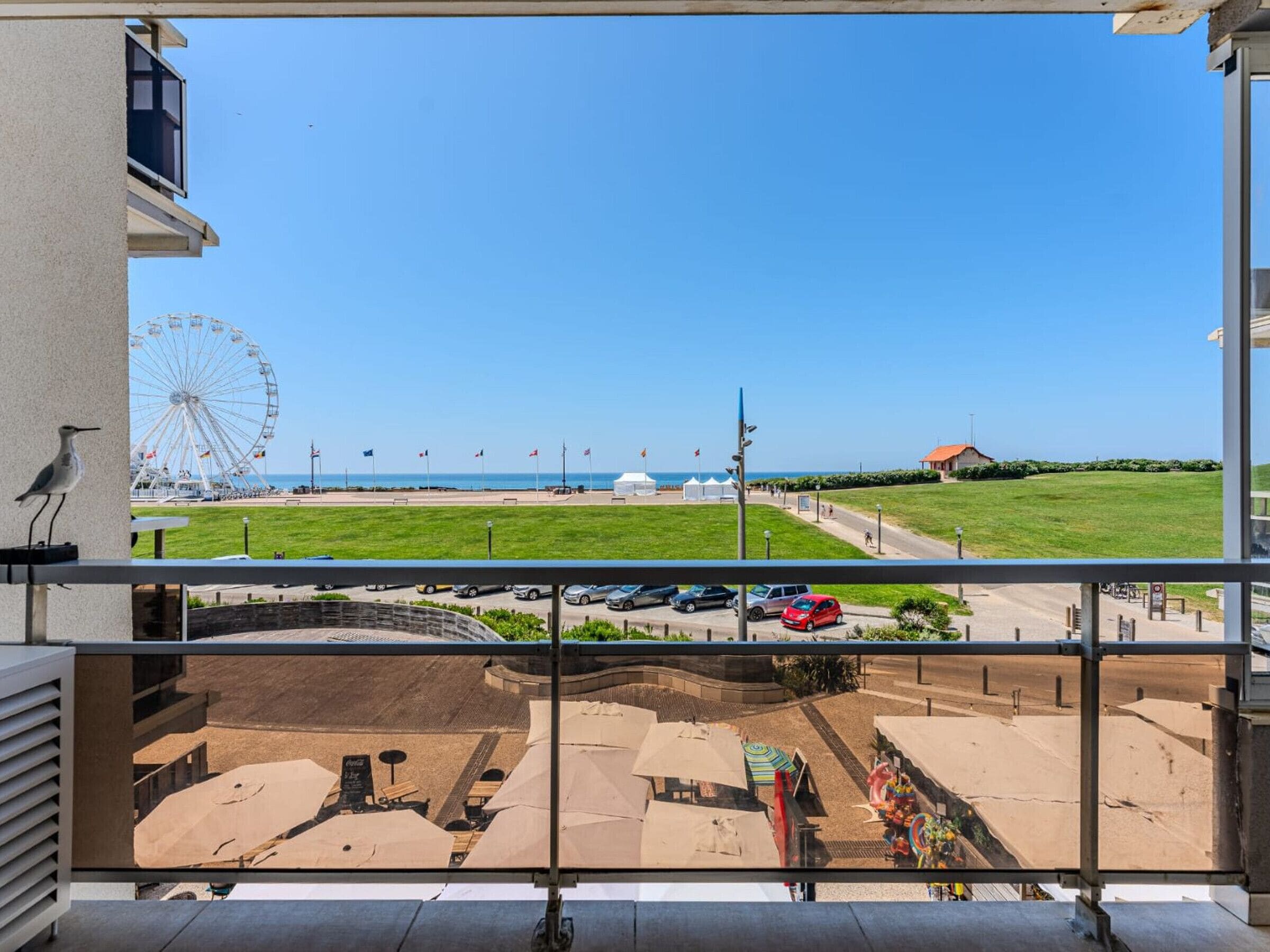 A balcony with a view of a beach, a Ferris wheel, and a parking area.
