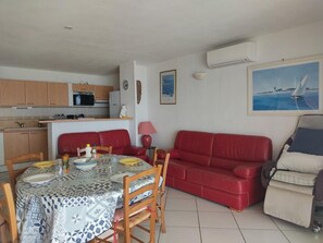 A compact living space with a dining area, a red sofa, and a painting of a sailboat. - Seaside T4 Villa in Gruissan, Air Conditioning, 80m2, Beach 50m, Sleeps 6. (Gruissan)