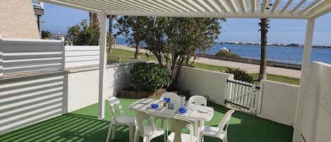 A covered patio with a table and chairs, a view of the sea, and a green artificial turf floor.