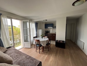 A compact living space with a dining area, kitchenette, and a balcony with curtains.