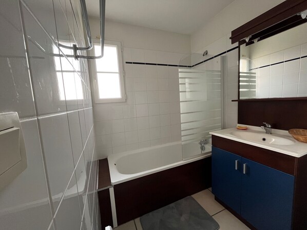 A modern bathroom with a glass shower enclosure, a white bathtub, and a vanity with a mirror.