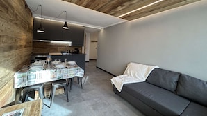 Une cuisine moderne avec un plafond en bois, une table à manger dressée avec des assiettes et des verres, et un canapé gris dans l’espace salon.