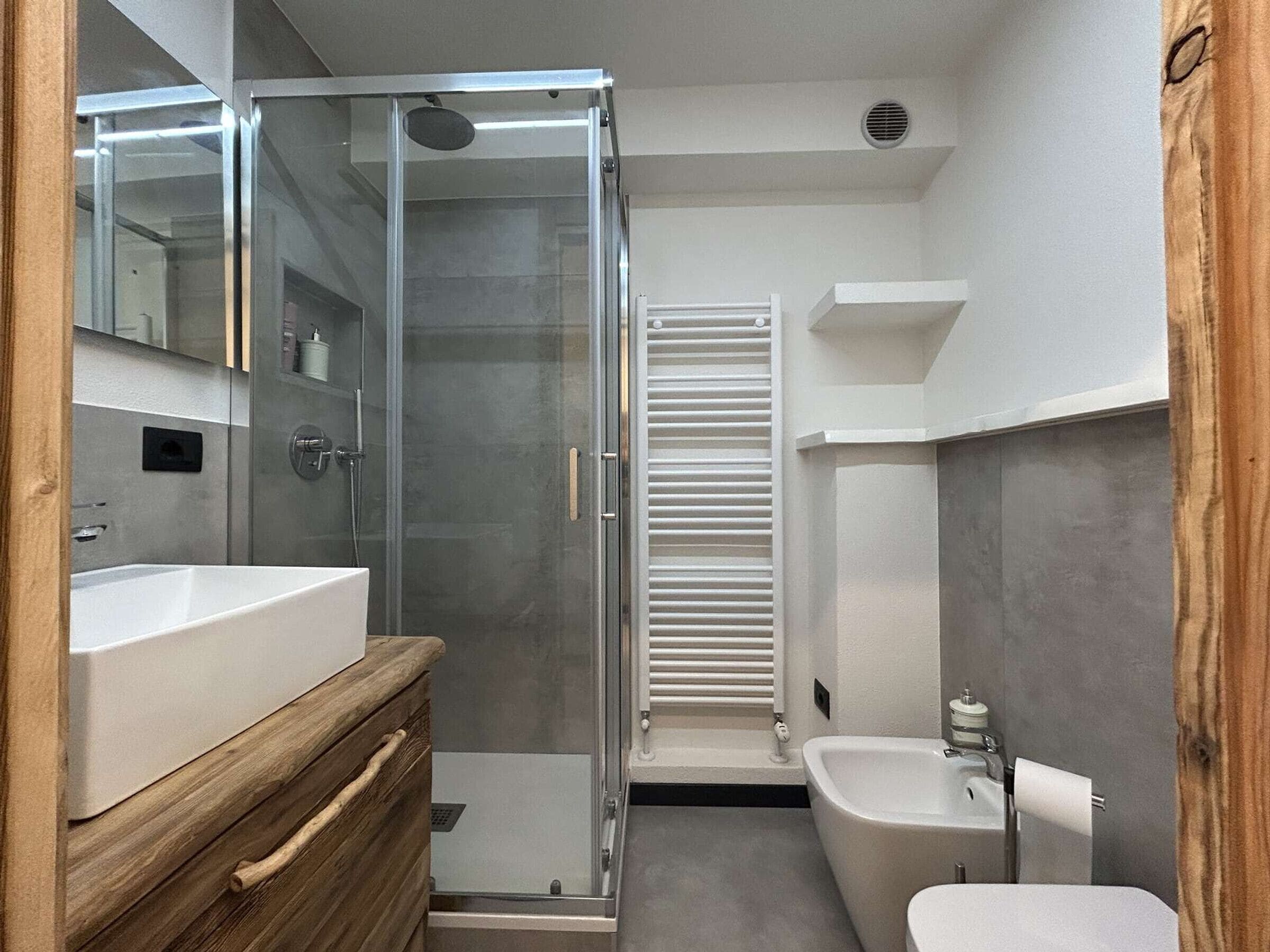 Un baño moderno con cabina de ducha de vidrio, tocador de madera, lavamanos blanco y bañera independiente.