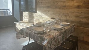 Un coin repas avec un mur en bois, un téléviseur fixé au-dessus de la table, et une table dressée avec des assiettes, des verres et une bouteille.