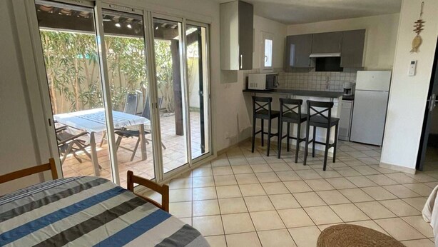 A room with a bed, a dining table, and a kitchen area with a refrigerator, microwave, and chairs. - Air-conditioned T3 Villa for 6 with pool and parking in Cap d'Agde (Cap d'Agde)