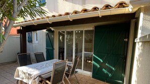 An outdoor patio with a table and chairs, a covered seating area, and a green door. - Air-conditioned T3 Villa for 6 with pool and parking in Cap d'Agde (Cap d'Agde)