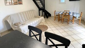 A living room with a sofa, a dining table with chairs, a staircase, and a TV mounted on the wall. - Air-conditioned T3 Villa for 6 with pool and parking in Cap d'Agde (Cap d'Agde)
